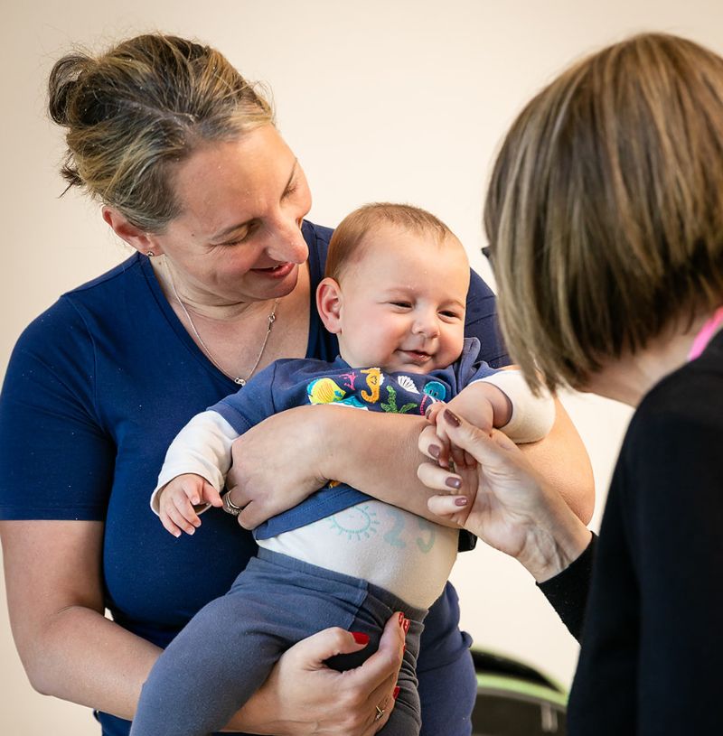 Baby Support Session Baby smiling while being held by a parent during a Mother to Mother support session.